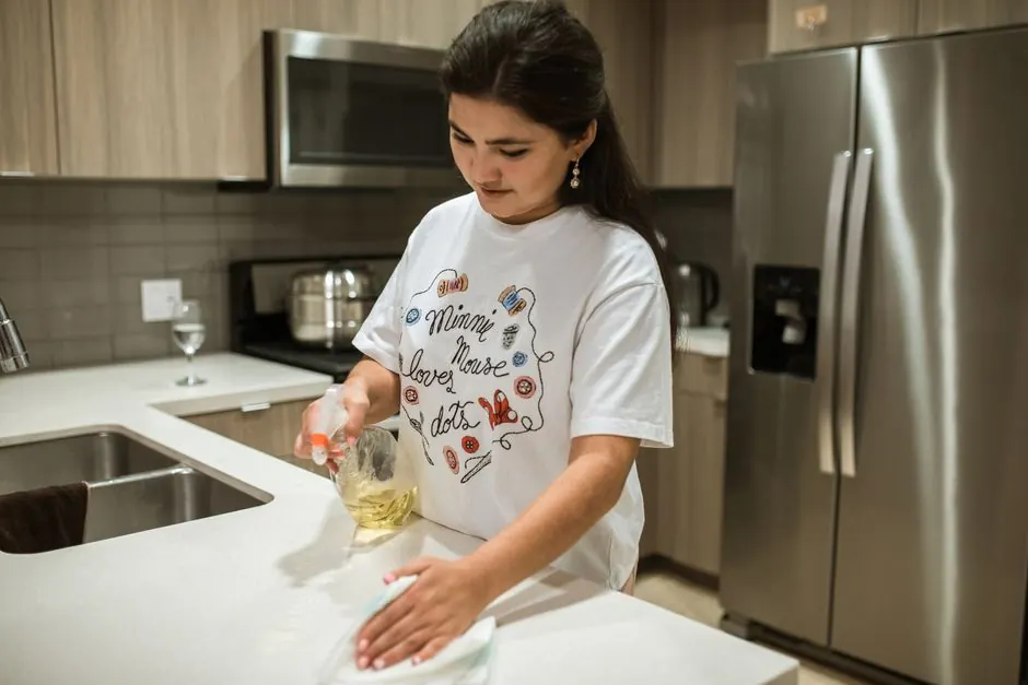Young woman cleaning a kitchen counter, wearing a Minnie Mouse T-shirt, indoors.